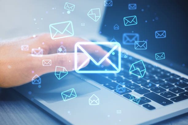 Close up of male hands using laptop keyboard on desk with glowing email letter icons on blurry background. Communication and business message concept